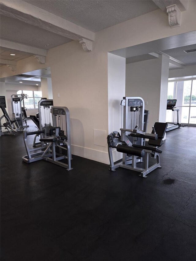 gym with a textured ceiling, visible vents, and baseboards