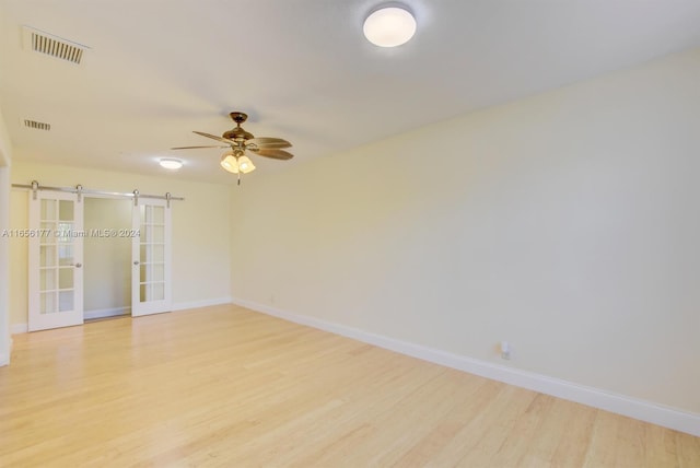 unfurnished room with light wood-type flooring, ceiling fan, and a barn door