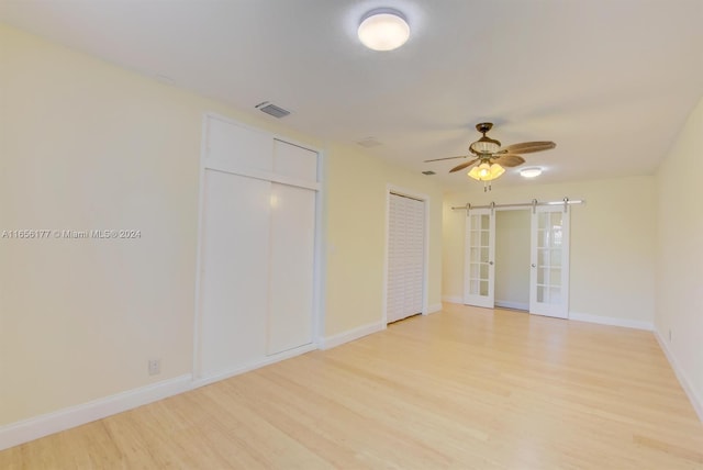 unfurnished bedroom with a barn door, ceiling fan, and light wood-type flooring