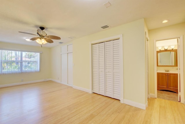 unfurnished bedroom with multiple closets, sink, ceiling fan, and light hardwood / wood-style floors