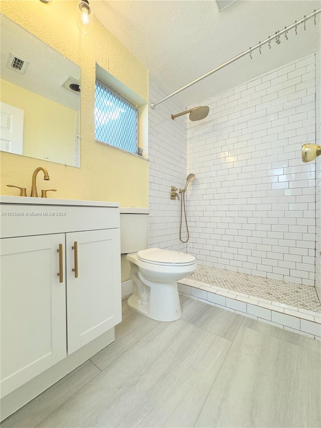 bathroom featuring toilet, a tile shower, a textured ceiling, and vanity