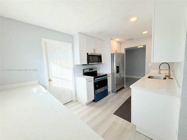 kitchen with appliances with stainless steel finishes, light hardwood / wood-style floors, white cabinetry, sink, and a textured ceiling