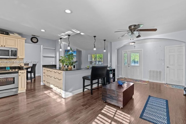 kitchen featuring ceiling fan, cream cabinets, decorative light fixtures, dark wood-type flooring, and appliances with stainless steel finishes