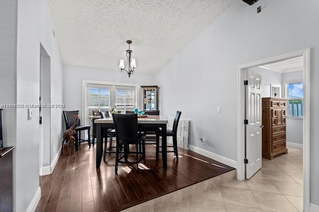 dining space with a textured ceiling, light hardwood / wood-style floors, an inviting chandelier, and lofted ceiling