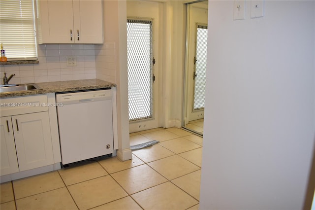 kitchen featuring a sink, dishwasher, white cabinetry, decorative backsplash, and light tile patterned floors