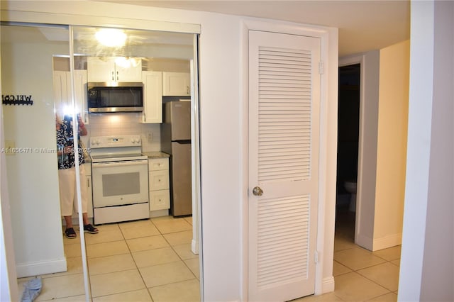 kitchen with white cabinets, light tile patterned flooring, stainless steel appliances, baseboards, and backsplash