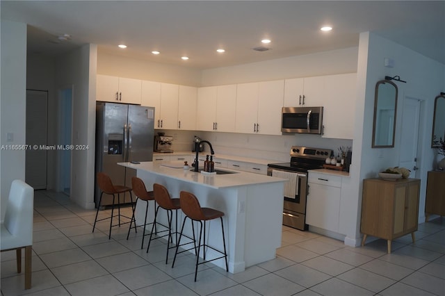 kitchen with light tile patterned flooring, white cabinets, stainless steel appliances, a kitchen bar, and a center island with sink