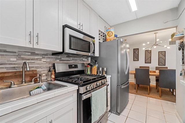 kitchen with an inviting chandelier, light tile patterned floors, appliances with stainless steel finishes, sink, and white cabinetry