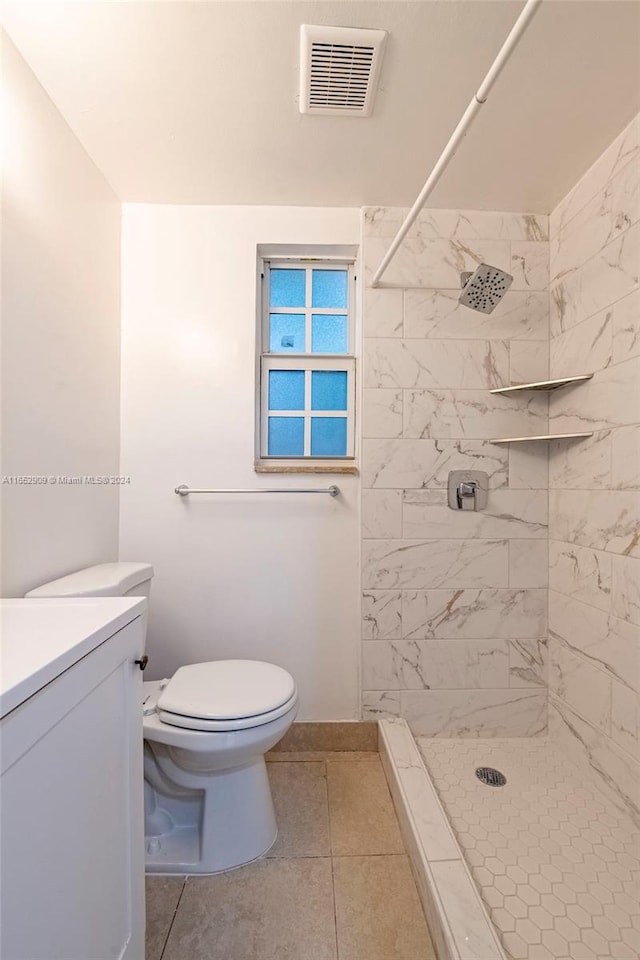 bathroom featuring vanity, toilet, a tile shower, and tile patterned flooring