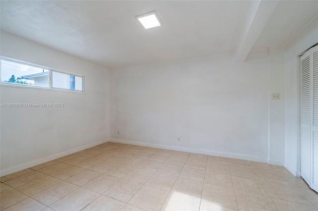 unfurnished bedroom featuring a closet, beam ceiling, and light tile patterned flooring