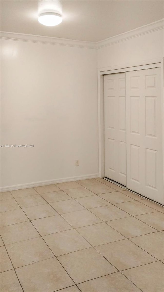 unfurnished bedroom featuring a closet, light tile patterned floors, and crown molding