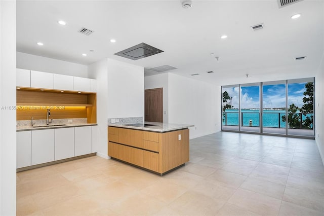 kitchen with light stone counters, white cabinetry, sink, expansive windows, and black electric stovetop