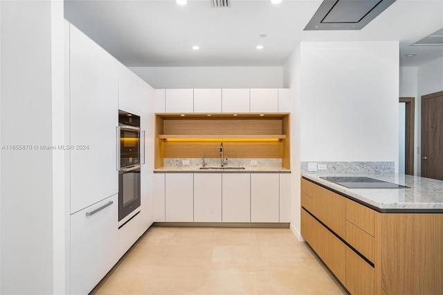 kitchen with black appliances, light stone counters, white cabinetry, and sink