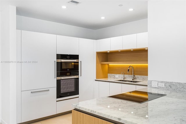 kitchen with double oven, light stone counters, white cabinetry, and sink