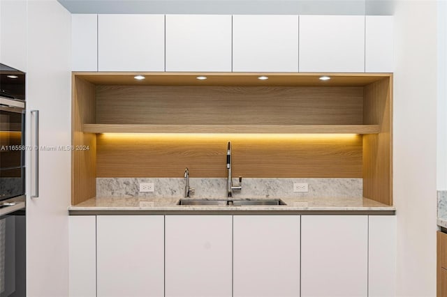 bar featuring oven, sink, light stone countertops, and white cabinets