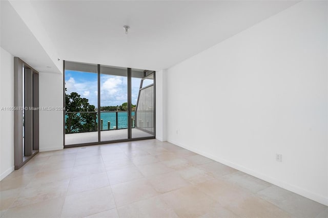 empty room featuring expansive windows, a water view, and light tile patterned flooring