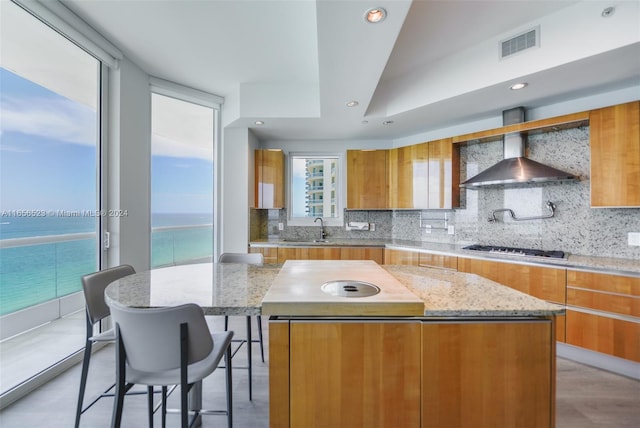 kitchen featuring a water view, decorative backsplash, a center island, and wall chimney exhaust hood