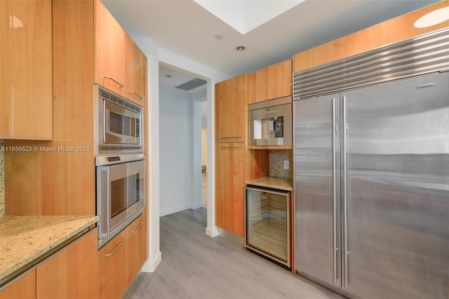 kitchen featuring light stone countertops, light hardwood / wood-style floors, beverage cooler, built in appliances, and decorative backsplash