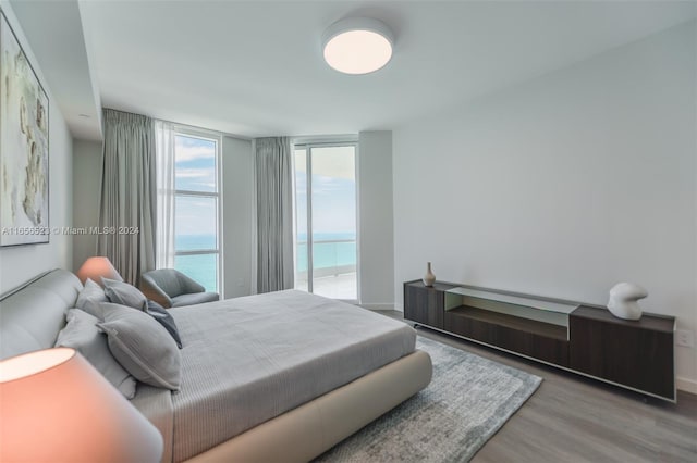 bedroom featuring floor to ceiling windows, access to exterior, wood-type flooring, and a water view