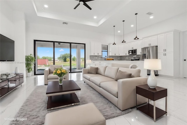 living room featuring a towering ceiling, ceiling fan, a tray ceiling, and sink