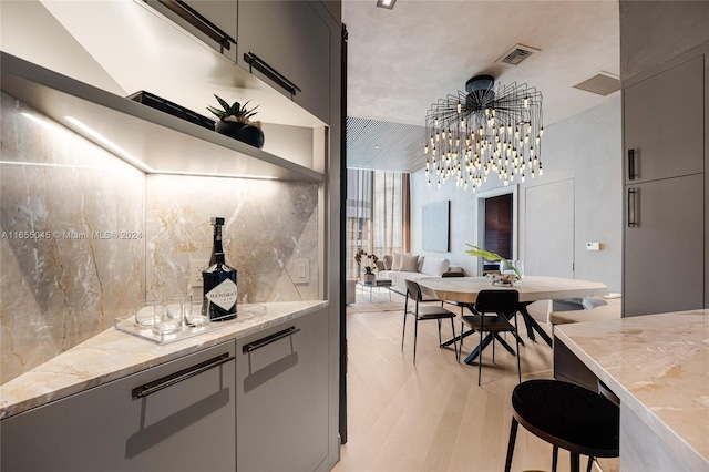 kitchen with pendant lighting, a breakfast bar, gray cabinets, light stone countertops, and tasteful backsplash