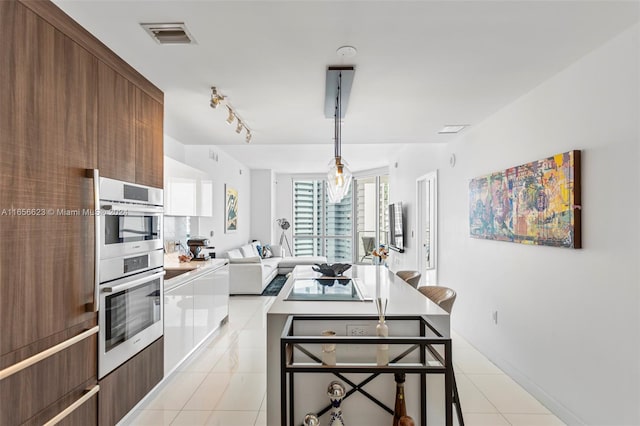 kitchen featuring light tile patterned floors, a kitchen bar, decorative light fixtures, and stainless steel double oven