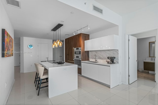 kitchen with white cabinetry, light tile patterned floors, a kitchen island, sink, and hanging light fixtures