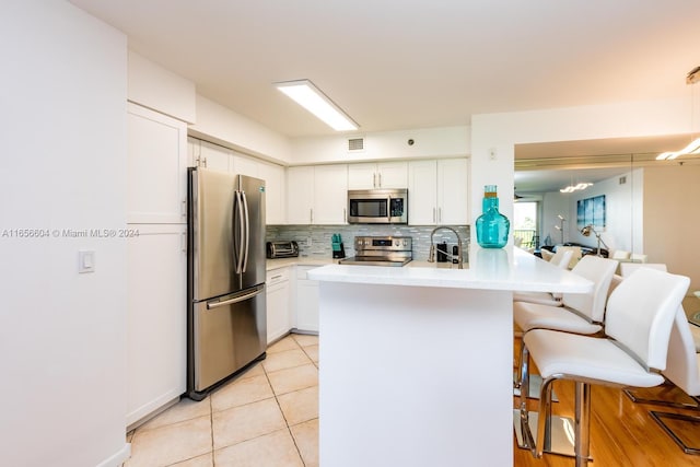 kitchen with white cabinets, decorative light fixtures, appliances with stainless steel finishes, kitchen peninsula, and a breakfast bar