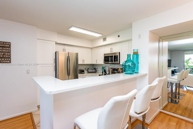 kitchen with white cabinets, stainless steel appliances, kitchen peninsula, and light hardwood / wood-style flooring