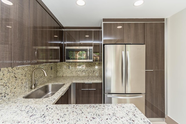 kitchen with backsplash, appliances with stainless steel finishes, light stone counters, sink, and dark brown cabinetry