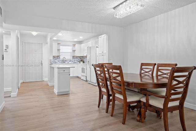 dining area featuring a textured ceiling, sink, a notable chandelier, and light hardwood / wood-style floors