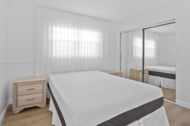 bedroom with multiple windows, a textured ceiling, light hardwood / wood-style floors, and a closet