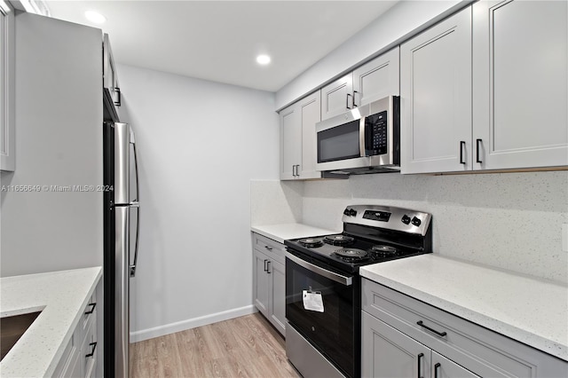 kitchen featuring gray cabinetry, tasteful backsplash, stainless steel appliances, light stone counters, and light wood-type flooring