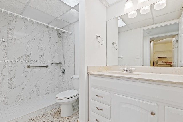 bathroom with toilet, tile patterned flooring, a drop ceiling, vanity, and a tile shower