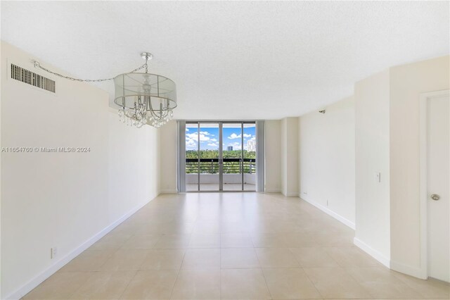 spare room with an inviting chandelier, light tile patterned floors, floor to ceiling windows, visible vents, and baseboards
