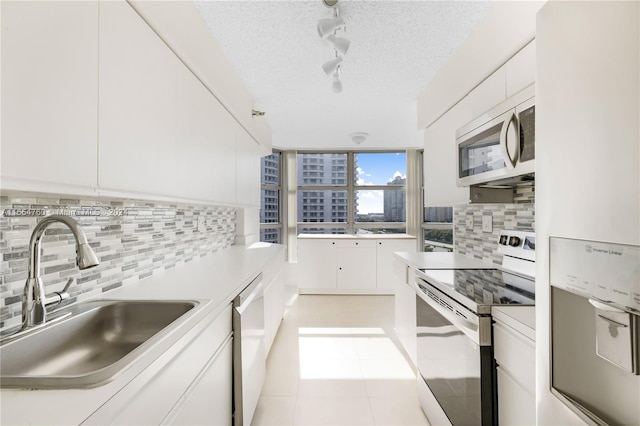 kitchen with white appliances, a textured ceiling, backsplash, sink, and white cabinets