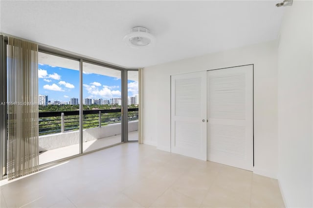 unfurnished bedroom with floor to ceiling windows, a view of city, access to outside, and a closet