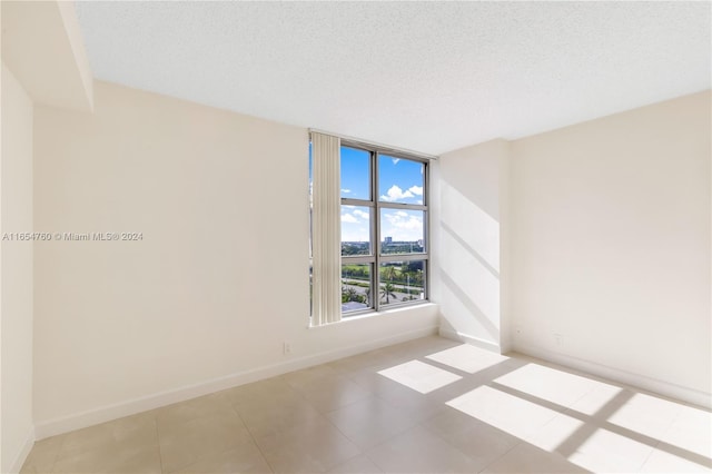 empty room featuring baseboards, a textured ceiling, and light tile patterned flooring
