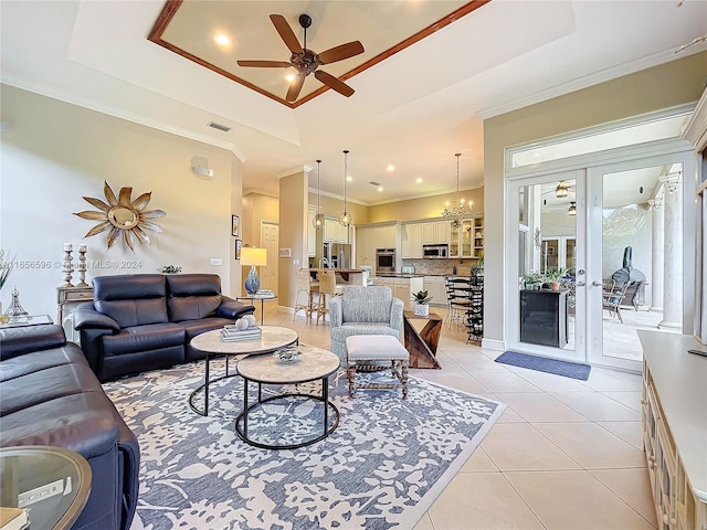 living room featuring a tray ceiling, ornamental molding, light tile patterned floors, and ceiling fan with notable chandelier