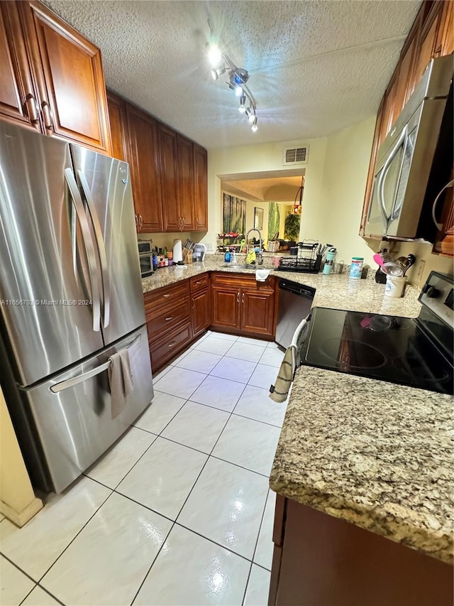 kitchen with light tile patterned floors, light stone counters, stainless steel appliances, kitchen peninsula, and a textured ceiling