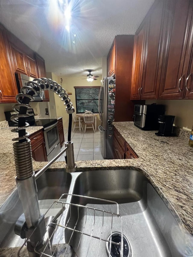 kitchen featuring tile patterned floors, a textured ceiling, light stone counters, ceiling fan, and appliances with stainless steel finishes