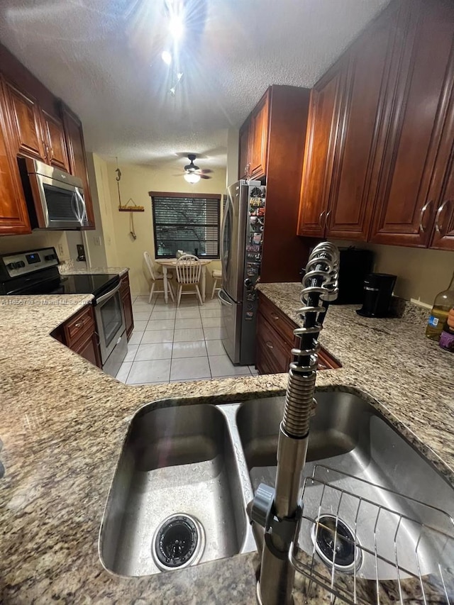 kitchen with light tile patterned floors, stainless steel appliances, sink, ceiling fan, and a textured ceiling