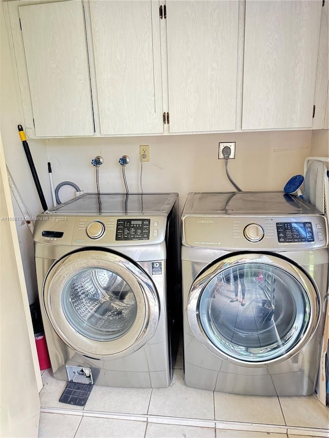 clothes washing area featuring separate washer and dryer, cabinets, and light tile patterned flooring