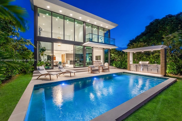 back house at twilight featuring a balcony, a yard, a patio, and area for grilling