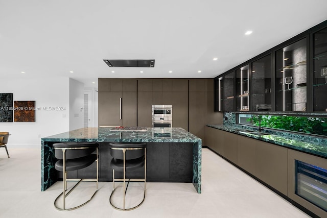 kitchen featuring backsplash, sink, a spacious island, dark stone counters, and a breakfast bar