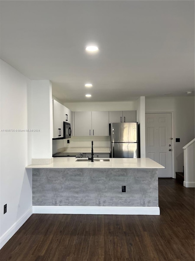 kitchen featuring dark hardwood / wood-style floors, kitchen peninsula, stainless steel refrigerator, sink, and white cabinetry