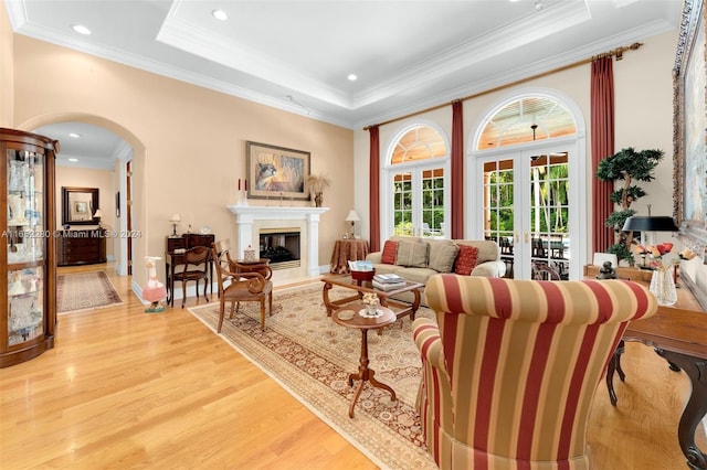 living room featuring a raised ceiling, a fireplace, crown molding, french doors, and hardwood / wood-style flooring