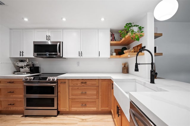 kitchen with stainless steel appliances, white cabinets, light wood-type flooring, and sink