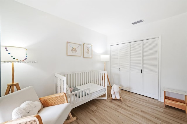 bedroom with a crib, a closet, and light hardwood / wood-style floors