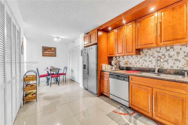 kitchen with sink, light tile patterned floors, stainless steel appliances, tasteful backsplash, and dark stone counters